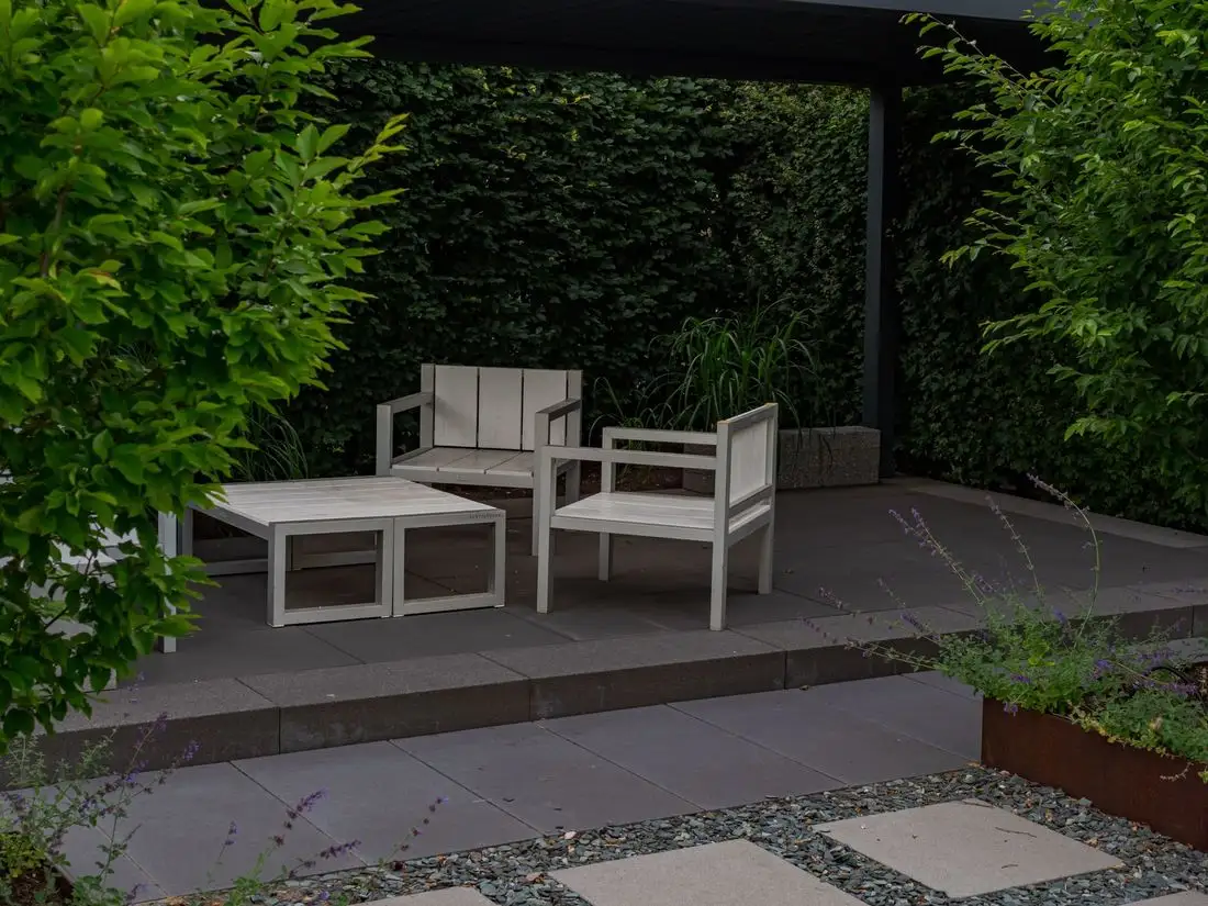 Concrete patio with outdoor furniture against a green hedge