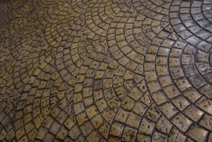 Stone cobbles laid in overlapping fan arcs, the kind of pattern stencilled concrete imitates